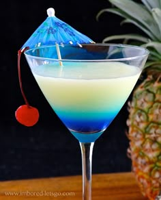 a blue and white drink in a martini glass next to a pineapple