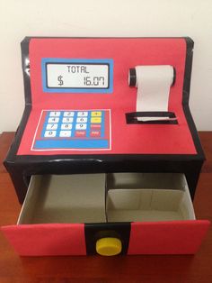 a toy cash register machine sitting on top of a wooden table next to a roll of toilet paper