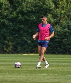 a man in pink and blue playing soccer on the grass with trees in the background