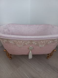 a pink bath tub with tassels and beads on the rim, sitting on a wooden floor