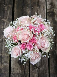 a bouquet of pink roses and baby's breath on a wooden table with white flowers