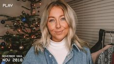 a woman standing in front of a christmas tree wearing a denim jacket and white shirt