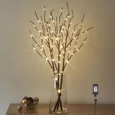 a vase filled with branches and lights on top of a wooden table next to a radiator