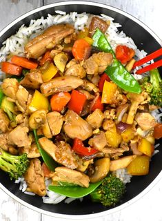 a black bowl filled with chicken and veggies on top of rice next to chopsticks