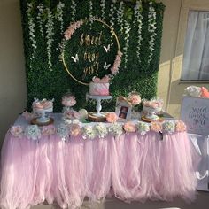 a table topped with lots of cake and cupcakes next to a wall covered in greenery