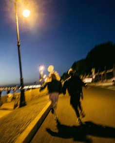 two people are running down the street at night, one is on his skateboard