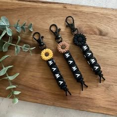 three keychains with flowers on them sitting on a wooden board next to plants