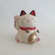 a ceramic cat figurine sitting on top of a white surface with a red ribbon around it's neck