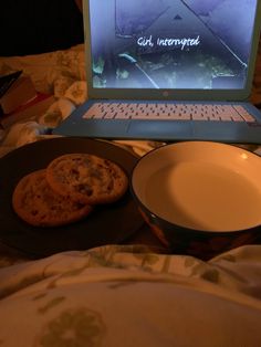 an open laptop computer sitting on top of a bed next to two plates with cookies