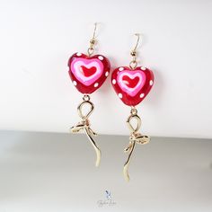 These unique lamp worked glass heart earrings feature cute red lamp work glass bead with 18k gold plate bowtie dangle drop charm and stainless steel ear wire. The elegant lamp work heart glass bead and bowtie earrings are the perfect gift for your loved on Valentine's occasion, a sweet heart for your sweetheart. Add these unique lollipop heart earrings to your everyday fashion earrings collection and match with your daily outfit to make a great statement. Dimensions: 2.77 x 0.78 inMaterial: Lamp worked glass, gold plated brass, stainless steel Jewelry Care: See more information about how to care for your jewelry here. Shipping Policy: Orders will be shipped within 1-3 business days. Economy shipping will take 7-14 days to arrive and standard shipping is 1- 4 days for U.S. orders. Internati Whimsical Red Jewelry For Valentine's Day, Red Whimsical Jewelry For Gift, Whimsical Red Jewelry For Gift, Whimsical Red Jewelry For A Gift, Cute Jewelry For Valentine's Day Party, Whimsical Red Party Jewelry, Cute Valentine's Day Party Jewelry, Elegant Red Heart Earrings For Gift, Whimsical Drop Earrings For Valentine's Day