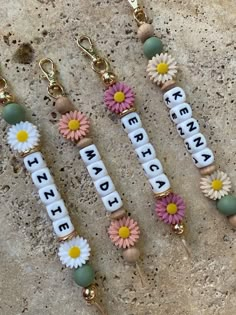 three key chains with flowers and letters on them sitting next to each other in front of a stone wall