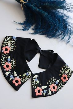 a black bandana with pink flowers and green leaves on it next to a blue feather