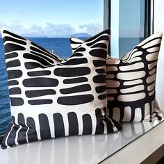 two black and white pillows sitting on top of a window sill next to the ocean