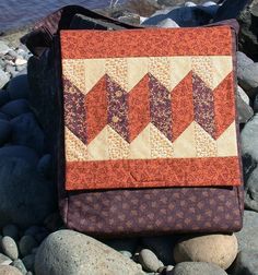 an orange and brown quilted bag sitting on rocks by the water's edge