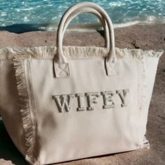 a white purse sitting on top of a sandy beach next to the ocean and water