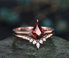 a close up view of a ring with a red stone in the middle and two white diamonds on top