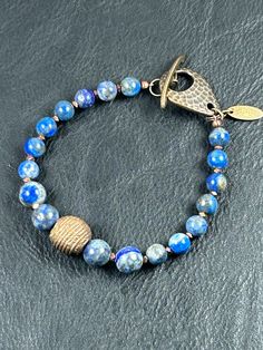 This Lapis beaded bracelet has a 10mm centerpiece bead of lost wax brass flanked by 8mm lapis beads & accompanied by 6mm lapis beads with copper spacer beads & a hammered antique brass toggle clasp.  The bracelet is 8 inches in circumference. Hand-strung Brass Bracelets With Round Beads, Brass Beaded Bracelets With Round Beads, Adjustable Bronze Jewelry With Polished Beads, Handmade Brass Bracelets With Round Beads, Handmade Brass Round Beaded Bracelets, Bronze Brass Bracelets With Round Beads, Handmade Blue Brass Bracelets, Bracelets Hippie, Chrysanthemum Stone