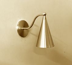 a wall mounted light on the side of a white wall with a cone shaped shade