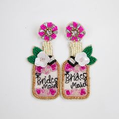 two beaded earrings with pink flowers and green leaves on the bottom one has a bride's maid tag attached to it