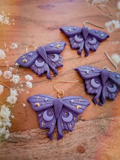 three purple butterfly shaped earrings sitting on top of a wooden table