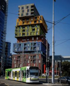 a green and white bus driving down a street next to tall buildings with balconies on top