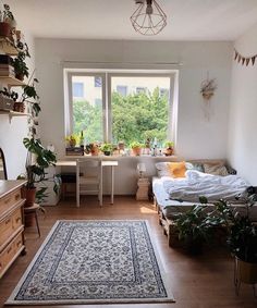 a room with a bed, desk and plants on the windowsills in it