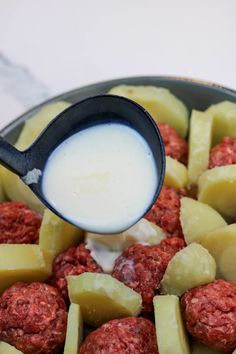 a ladle scooping milk over meatballs and potatoes