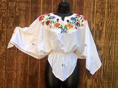 "An ethnic, summer festive blouse that is embellished with floral embroidery.  No tags - estimated size medium - please see measurements. Good vintage condition.   Measurements taken across front laid flat Bustbatwing\" Shoulder to waist18\" Waiststretches from 12\" to 21\" across front" Spring Traditional Tops With Boho Collar, Traditional Fitted Peasant Top With Floral Embroidery, Fitted Embroidered Traditional Peasant Top, Festive Summer Tops With Embroidered Border, Bohemian Fitted Blouse With Embroidered Border, Traditional Embroidered Top For Beach In Spring, Traditional Peasant Top For Summer Vacation, Fitted Traditional Embroidered Peasant Top, Traditional Embroidered Blouse For Vacation