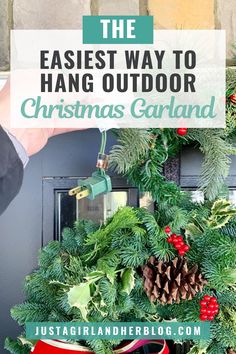 Person holding an outdoor Christmas garland with holly, pinecones, and berries while preparing to hang it around a front door, illustrating how to hang outdoor Christmas garland for holiday decorations. Patio Door Christmas Decor, Garland On Front Porch Pillars, Christmas Front Door Garland Ideas, Fence Garland Christmas, Garage Door Christmas Decoration Ideas, Pine Garland Christmas Front Porches, Christmas Doorway Decorations Outdoor, How To Hang Garland On Brick House, Christmas Porch Garland