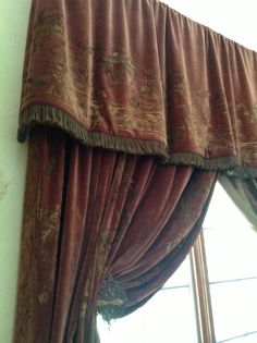 the curtain is hanging on the side of the window with an ornate pattern and gold trim