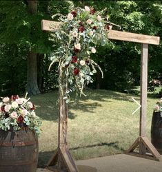 an outdoor ceremony setup with flowers and greenery on the top, along with two wooden barrels