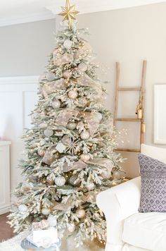 a white christmas tree with silver and gold ornaments on it in a living room area