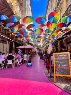 many colorful umbrellas hanging from the ceiling in an open market area with people sitting at tables