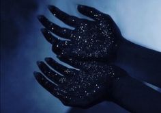 a person's hand with black glitter on it in the dark, against a blue background