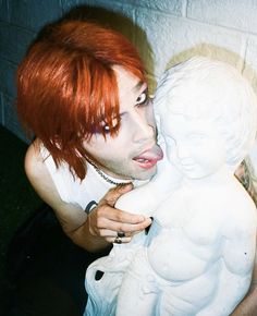 a woman with red hair and piercings on her face is holding a statue of a child