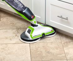 a green and white steam mop sitting on the floor in front of a cabinet