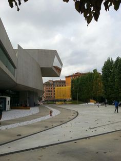 two people walking in front of a building with an open courtyard and trees on the other side