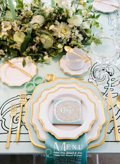 the table is set with gold and white plates, silverware, and green napkins