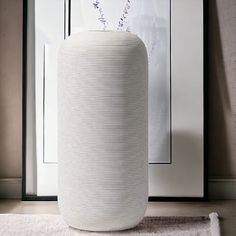 a large white vase sitting on top of a rug next to a framed picture and plant