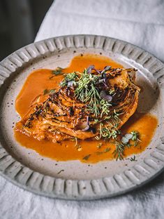 a white plate topped with meat covered in gravy and garnished with herbs