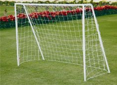 a soccer goal on the grass with flowers in the backgroung behind it