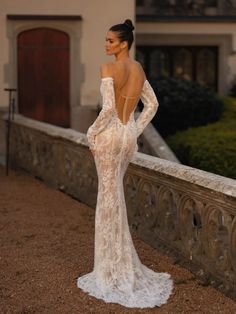 a woman in a white wedding dress standing on a stone wall with her back to the camera