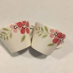 two white cups with pink flowers on them sitting next to each other in front of a white background