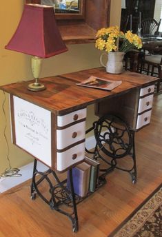 an old sewing machine turned into a desk with flowers on it and a lamp next to it