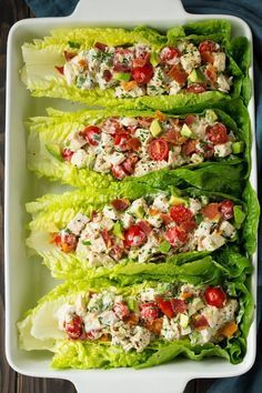 four lettuce wraps with tomatoes and chicken on them in a white serving dish