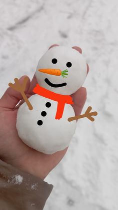 a hand holding a small snowman made out of white rocks with orange scarf and carrots on it