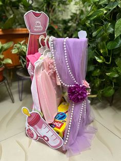 a pink and purple gift basket filled with baby's clothes, toys, and other items