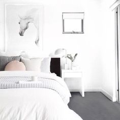 a white bedroom with a horse painting on the wall next to it's bed