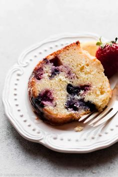 a piece of cake on a white plate with a fork next to it and a strawberry