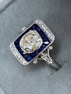 ART DECO RING with a 1.48ct Old Mine Brilliant center diamond . The ring is a newer mounting made with 1.15ct of natural blue sapphires custom cut to fit around the center diamond. There are also .15ct of small accent diamonds going down the detailed sides of the ring. Wonderfully crafted. A blend of old and new. Finger Size 6.5 in 14k White gold. ALL NATURAL DIAMONDS. NOT LAB GROWN. Art Deco Sapphire Ring, Antique Engagement, Deco Ring, Antique Engagement Rings, Natural Blue Sapphire, Fantasy Jewelry, Art Deco Ring, Belle Epoque, Vintage Diamond